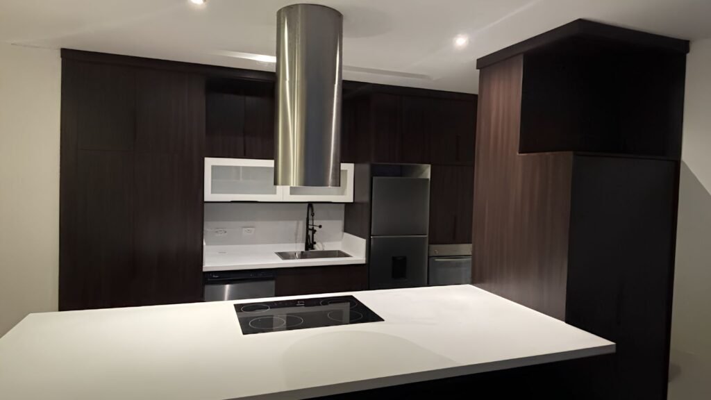 Cocina con gabinetes en tono madera oscuro, isla blanca y campana de acero inoxidable