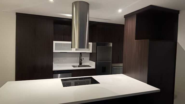 Cocina con gabinetes en tono madera oscuro, isla blanca y campana de acero inoxidable
