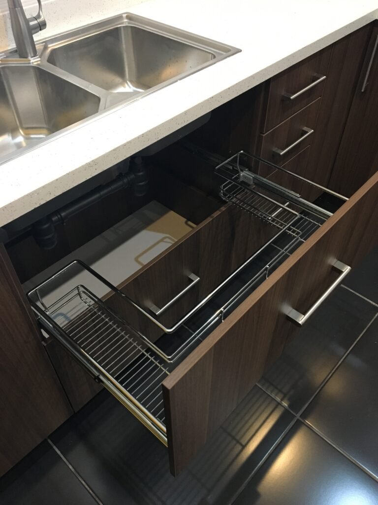 Interior del gabinete bajo el lavatrastos, con tuberías y conexiones visibles